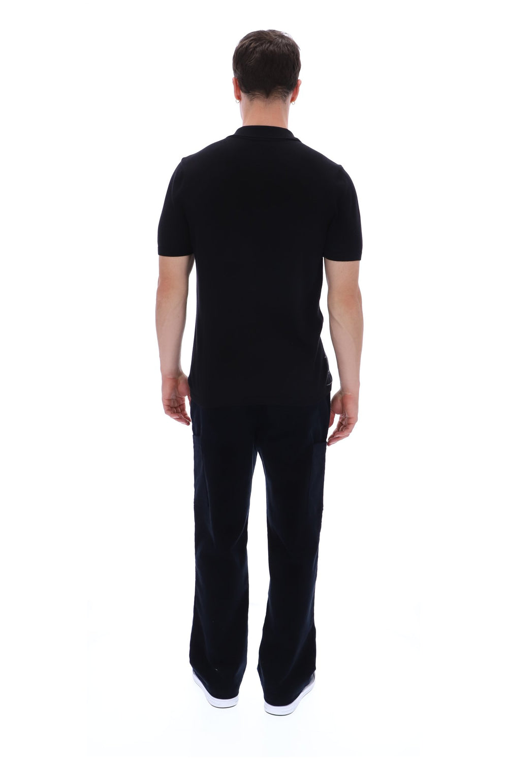 A man viewed from the back wearing a black short-sleeve polo shirt and matching black trousers, standing against a plain white studio background.