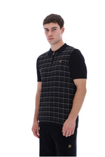 A man modeling a black short-sleeve polo shirt with a white windowpane plaid pattern on the front panel and a small gold logo on the chest, set against a plain white background.