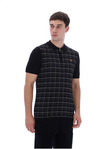A man wearing a black short-sleeve polo shirt with a white windowpane plaid pattern on the front panel and a small gold embroidered logo on the chest, photographed against a plain white background.