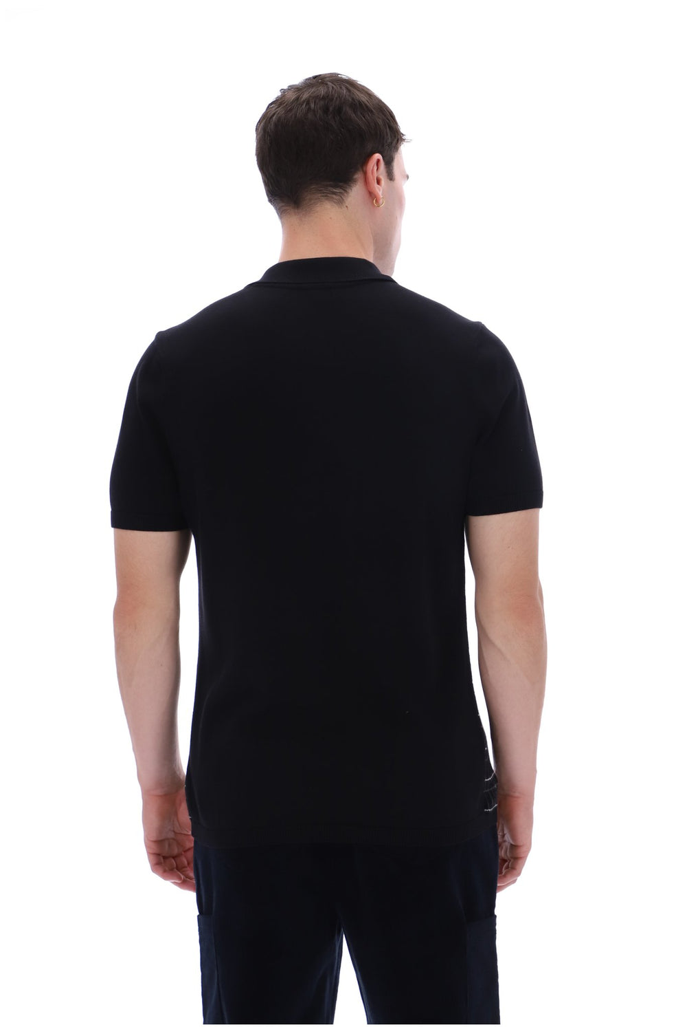 A man viewed from the back wearing a black short-sleeve polo shirt and dark trousers against a plain white studio background.
