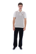 A man modeling a short-sleeve polo shirt with a beige and white plaid pattern on the body and white sleeves, paired with black trousers and black sneakers, against a solid white background.