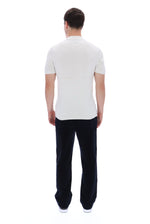 A man viewed from behind wearing a white short-sleeve polo shirt and dark navy trousers, standing against a plain white background.