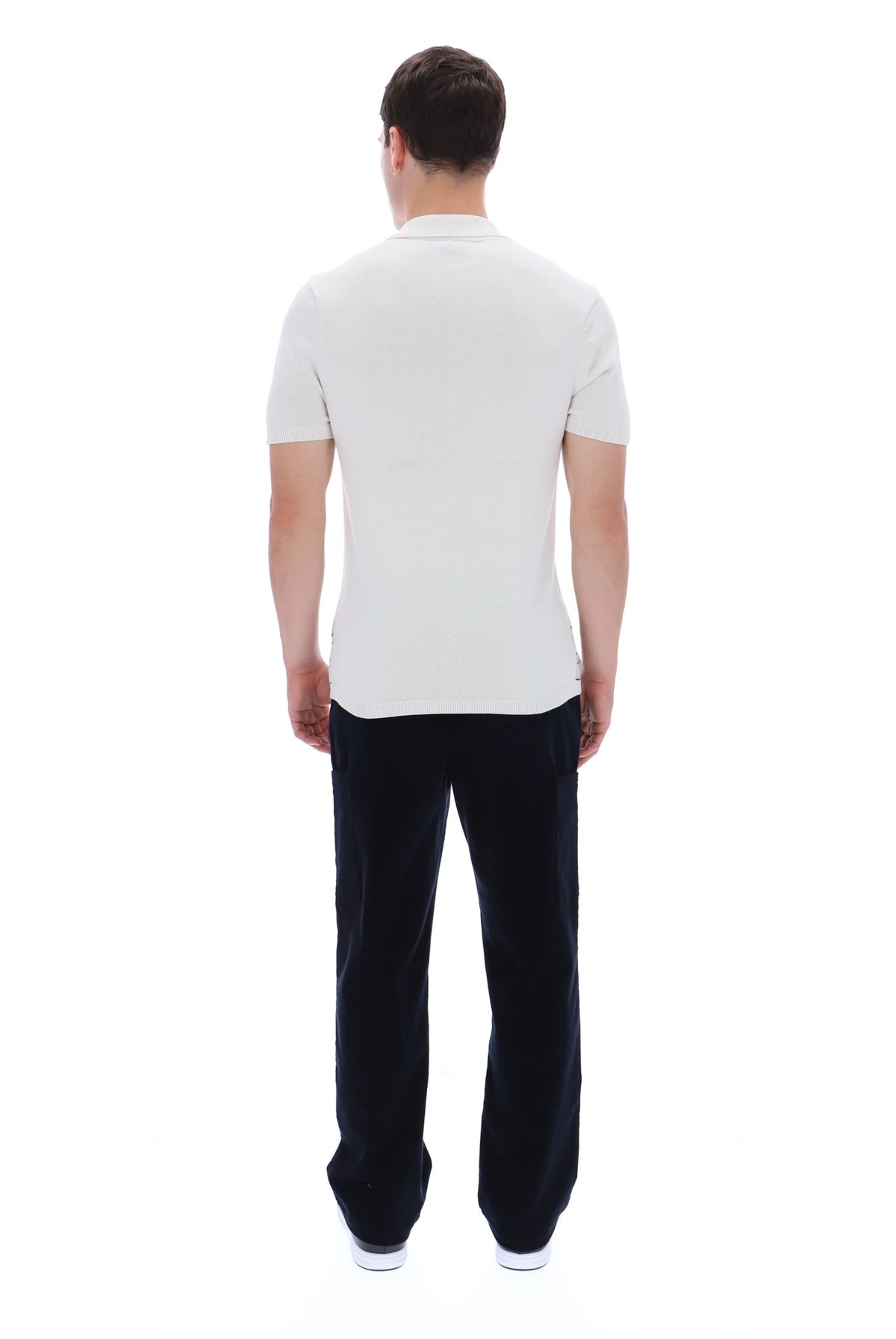 A man viewed from behind wearing a white short-sleeve polo shirt and dark navy trousers, standing against a plain white background.