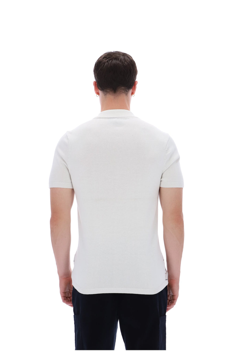 A man viewed from the back wearing a fitted short-sleeve polo shirt in off-white and dark trousers, against a plain white studio background.