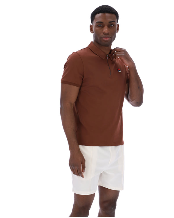 Man wearing a brown FILA polo shirt and white shorts on a white background