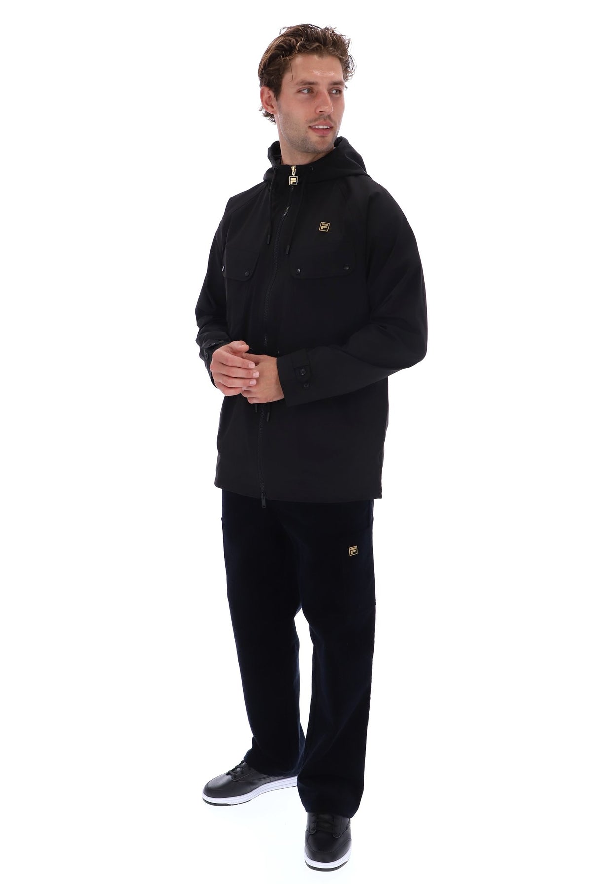 A man modeling a black hooded jacket and matching black pants against a plain white background.