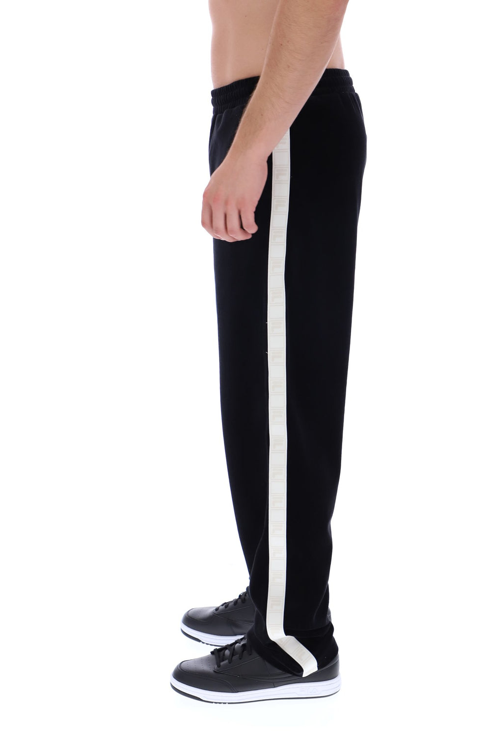 A side-profile view of a person wearing black track pants with a prominent white vertical stripe down the side, paired with black sneakers, against a plain white background.