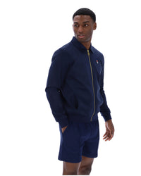 Man wearing a navy tracksuit jacket with a FILA logo on the chest, paired with matching shorts, on a white background