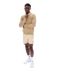 Man wearing a beige tracksuit Jacket with a small FILA logo on the chest, paired with cream shorts, on a white background