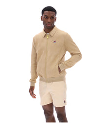 Man wearing a beige tracksuit Jacket with a small FILA logo on the chest, paired with cream shorts, on a white background
