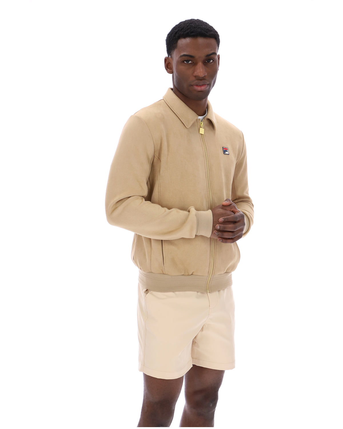 Man wearing a beige tracksuit Jacket with a small FILA logo on the chest, paired with cream shorts, on a white background