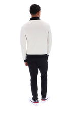 A man viewed from behind wearing a cream knit sweater with black ribbed trim, black trousers, and white sneakers with red accents, set against a plain white background.