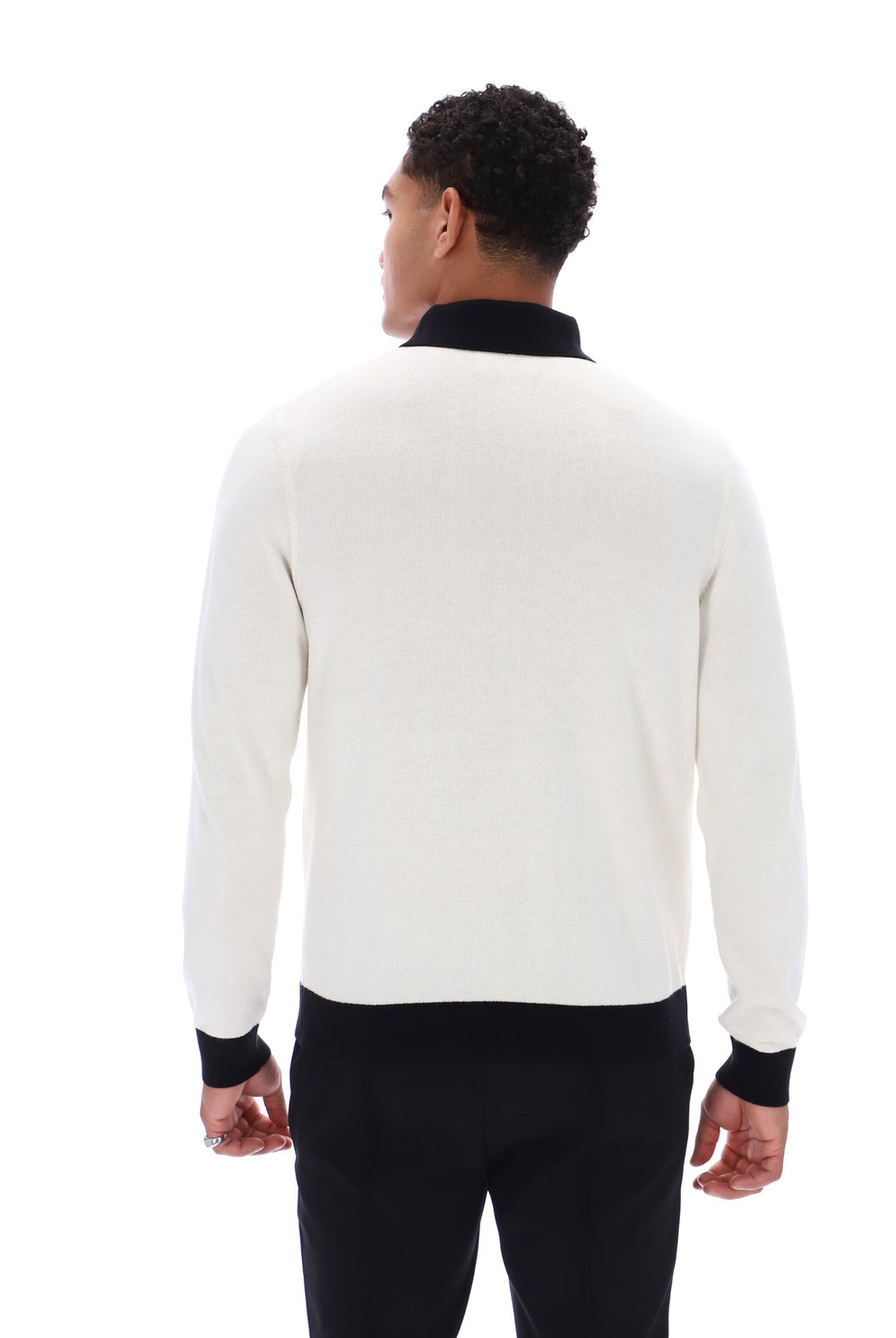 A man viewed from the back wearing a cream-colored knit sweater with black ribbed collar, cuffs, and hem, paired with black trousers, against a plain white background.
