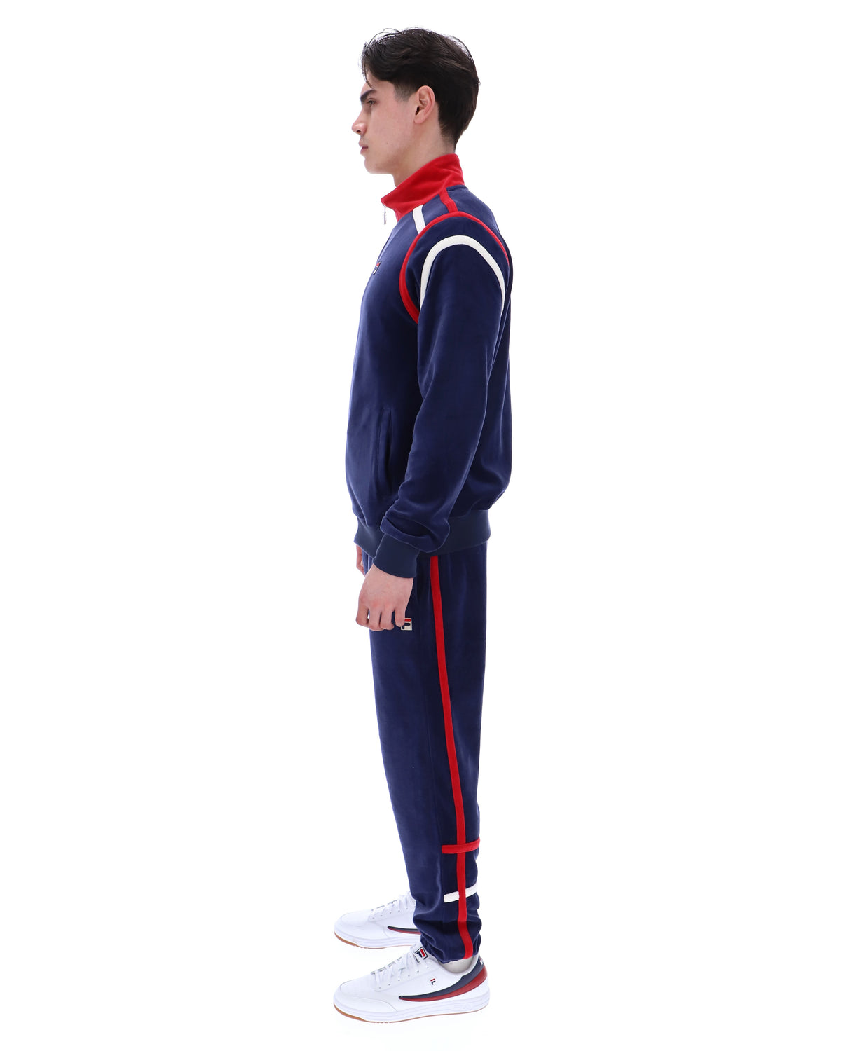 Man wearing a navy tracksuit with red and white accents, with a FILA logo on the chest, paired with matching bottoms, against a white background