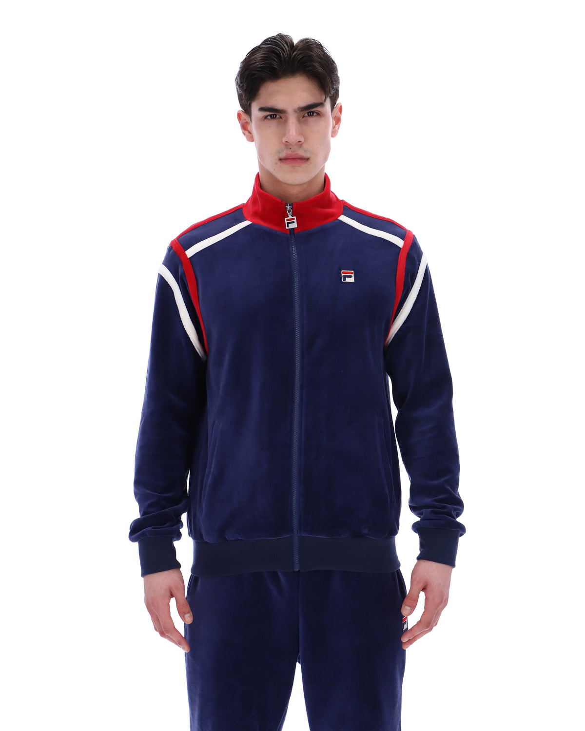 Man wearing a navy tracksuit with red and white accents, with a FILA logo on the chest, paired with matching bottoms, against a white background