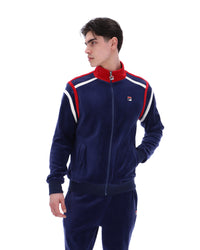 Man wearing a navy tracksuit with red and white accents, with a FILA logo on the chest, paired with matching bottoms, against a white background