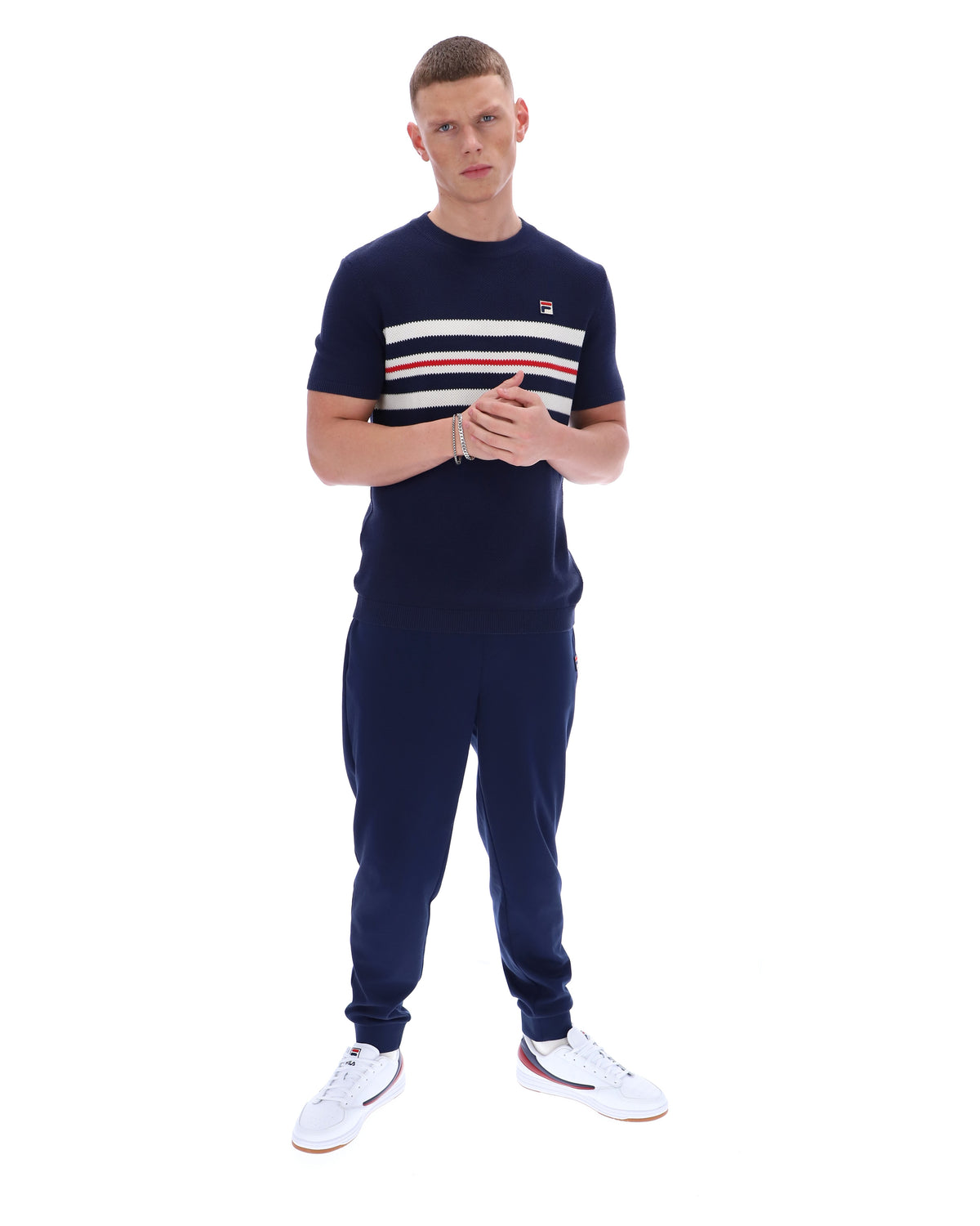 Man wearing a Navy blue t-shirt with white and red stripes and Fila logo with matching joggers on a white background