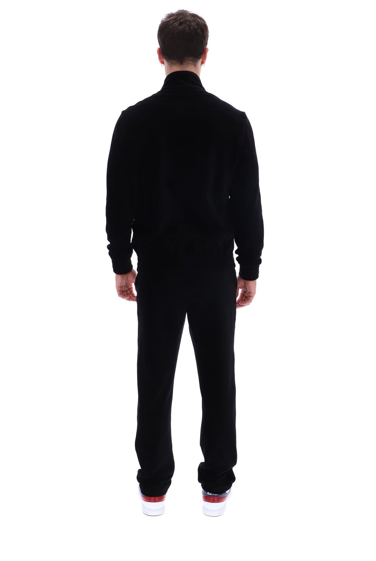 A man viewed from behind wearing a black long-sleeve mock-neck fleece jacket and matching black fleece pants, paired with white sneakers with red soles, against a solid white background.