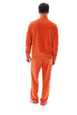 A man viewed from behind wearing a matching orange corduroy tracksuit with a zip-up jacket and pants, paired with white sneakers, against a plain white background.