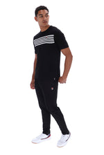 A man modeling a black short-sleeve t-shirt with three white horizontal stripes across the chest, paired with black joggers featuring a small red and white logo on the left thigh, and white sneakers, set against a plain white background.
