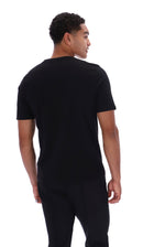 A man wearing a plain black short-sleeve t-shirt and black pants, photographed from the back against a solid white background.