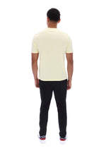 A man viewed from behind wearing a pale yellow short-sleeve t-shirt, black pants, and white sneakers with red accents, set against a plain white background.