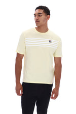 A man wearing a pale yellow short-sleeve t-shirt with white horizontal stripes across the chest and a small Fila logo on the left chest, paired with black pants, against a plain white background.
