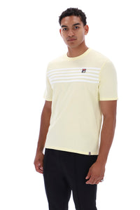 A man wearing a pale yellow Fila short-sleeve t-shirt with white horizontal stripes across the chest and a small red and blue logo, paired with black pants, against a plain white background.