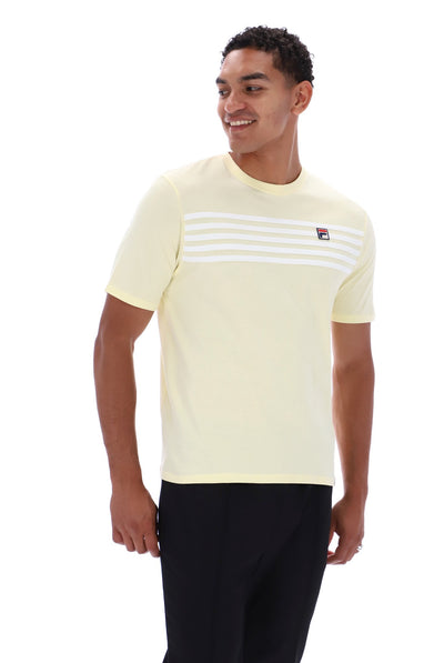 A man wearing a pale yellow short-sleeve t-shirt with white horizontal stripes across the chest and a small Fila logo, paired with black pants, against a plain white background.