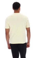 A man viewed from the back wearing a pale yellow short-sleeve crewneck t-shirt and black pants, set against a plain white background.