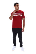 A man modeling a red short-sleeve t-shirt with three horizontal white stripes across the chest, paired with black pants and white sneakers, against a plain white background.
