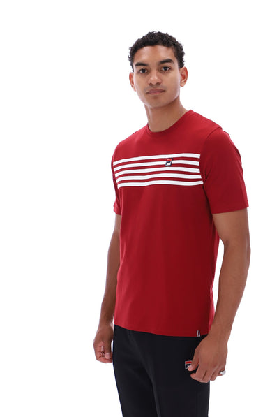 A man wearing a red short-sleeve crewneck t-shirt with horizontal white stripes across the chest and a small Tommy Hilfiger flag logo, paired with black pants, against a plain white background.