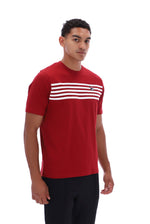 A man wearing a red short-sleeve athletic t-shirt with horizontal white stripes across the chest and a small logo on the right chest, paired with black pants, against a plain white background.