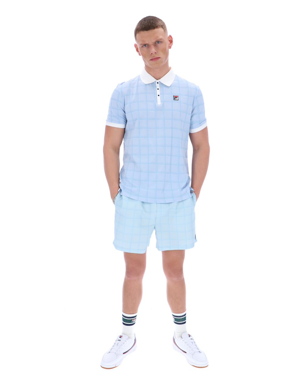 Man wearing a light blue checkered polo shirt and shorts set on a white background