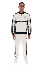 A man modeling a vintage Fila tracksuit in off-white and black, featuring a zip-up jacket and matching jogger pants, against a plain white background.