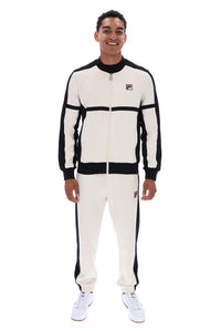 A man modeling a vintage Fila tracksuit in off-white and black, featuring a zip-up jacket and matching jogger pants, against a plain white background.