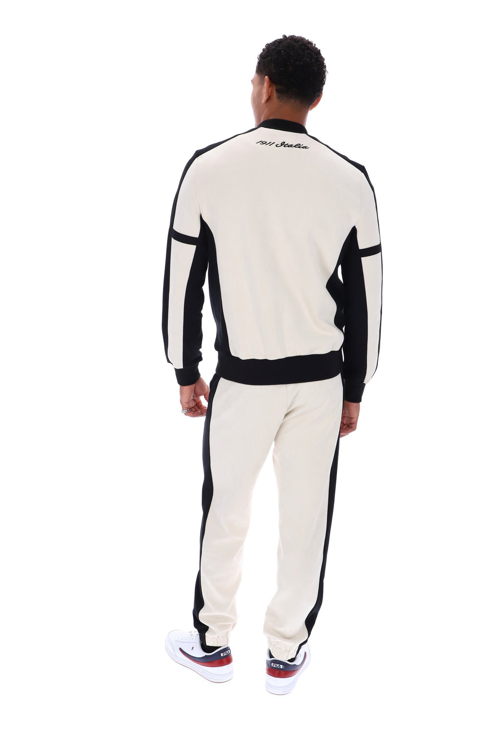 A man viewed from the back wearing a black and off-white tracksuit with matching sneakers, set against a plain white background.