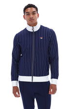 A man wearing a navy blue pinstriped zip-up jacket with white ribbed trim and a small Fila logo on the chest, paired with navy pants, against a plain white background.