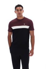 A man modeling a short-sleeve crewneck t-shirt by FILA, featuring a color-blocked design with a burgundy top, a wide white stripe across the chest, and a black lower body. He is also wearing black sweatpants against a solid white background.