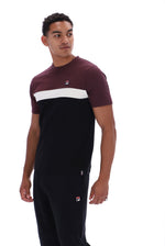 A man wearing a color-blocked short-sleeve t-shirt and matching sweatpants by Fila. The t-shirt features a maroon upper chest and shoulders, a wide white horizontal stripe across the chest, and a solid black lower body.