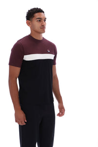 A man wearing a color-blocked short-sleeve t-shirt and matching dark trousers, standing against a plain white studio background. The t-shirt features a maroon upper section, a white horizontal stripe across the chest, and a small red and blue logo on the left chest.
