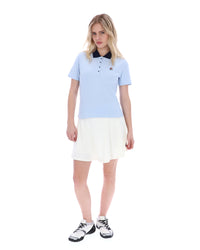 Woman wearing a light blue polo shirt and white skirt on a white background