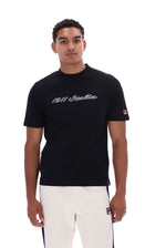 A man wearing a black short-sleeve t-shirt with '1911 Italia' written in white script across the chest, paired with white pants, photographed against a solid white background.