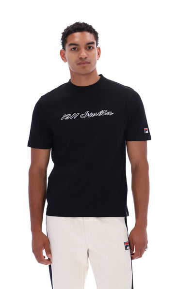 A man wearing a black short-sleeve t-shirt with '1911 Italia' written in white script across the chest, paired with white pants, photographed against a solid white background.