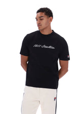 A man wearing a black short-sleeve t-shirt with '1911 Italia' written in white script across the chest, paired with white pants featuring a small Fila logo patch on the leg.
