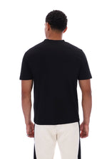 A man viewed from the back wearing a plain black short-sleeve crew-neck t-shirt and off-white pants with black side panels, against a solid white background.