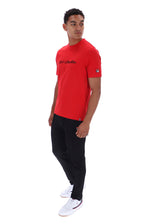 A man modeling a red short-sleeve t-shirt with black pants and white sneakers, standing against a plain white background.