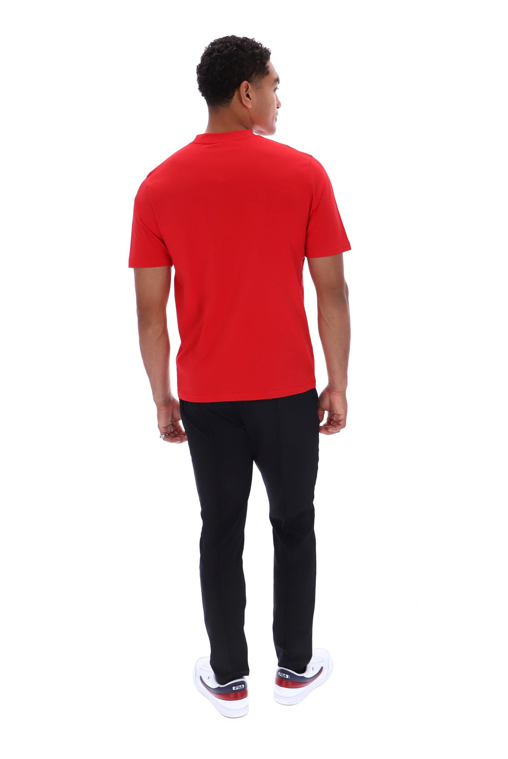 A man viewed from the back wearing a bright red short-sleeve t-shirt, black pants, and white sneakers with red accents, set against a plain white background.