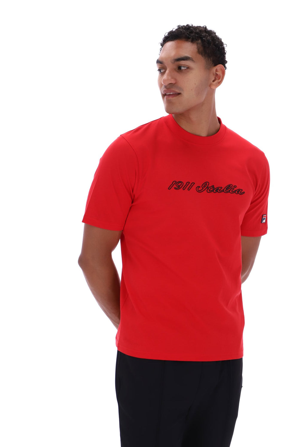 A man wearing a bright red short-sleeve t-shirt with '1911 Italia' written in black script across the chest, paired with black pants, photographed against a solid white background.