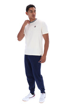 A man modeling a white short-sleeve crewneck t-shirt with a gray collar trim and a small red logo on the chest, paired with navy joggers and white sneakers, against a plain white background.